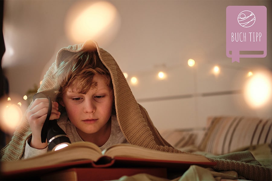 Junge unter Decke mit Taschenlampe Buch lesen